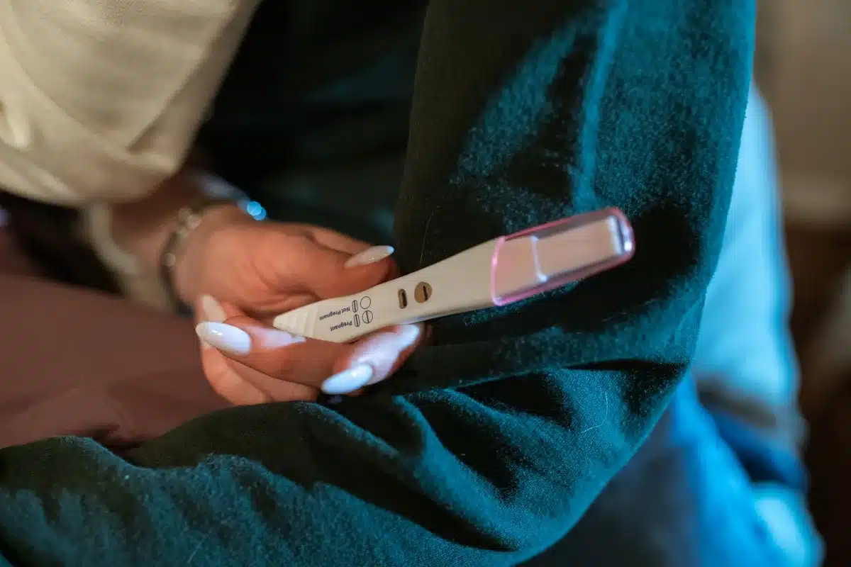 Donna che tiene un test di gravidanza positivo in una camera da letto moderna con luce naturale