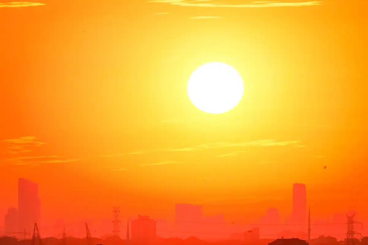 Termometro che segna temperature estreme con onde di calore visibili sopra l'asfalto urbano